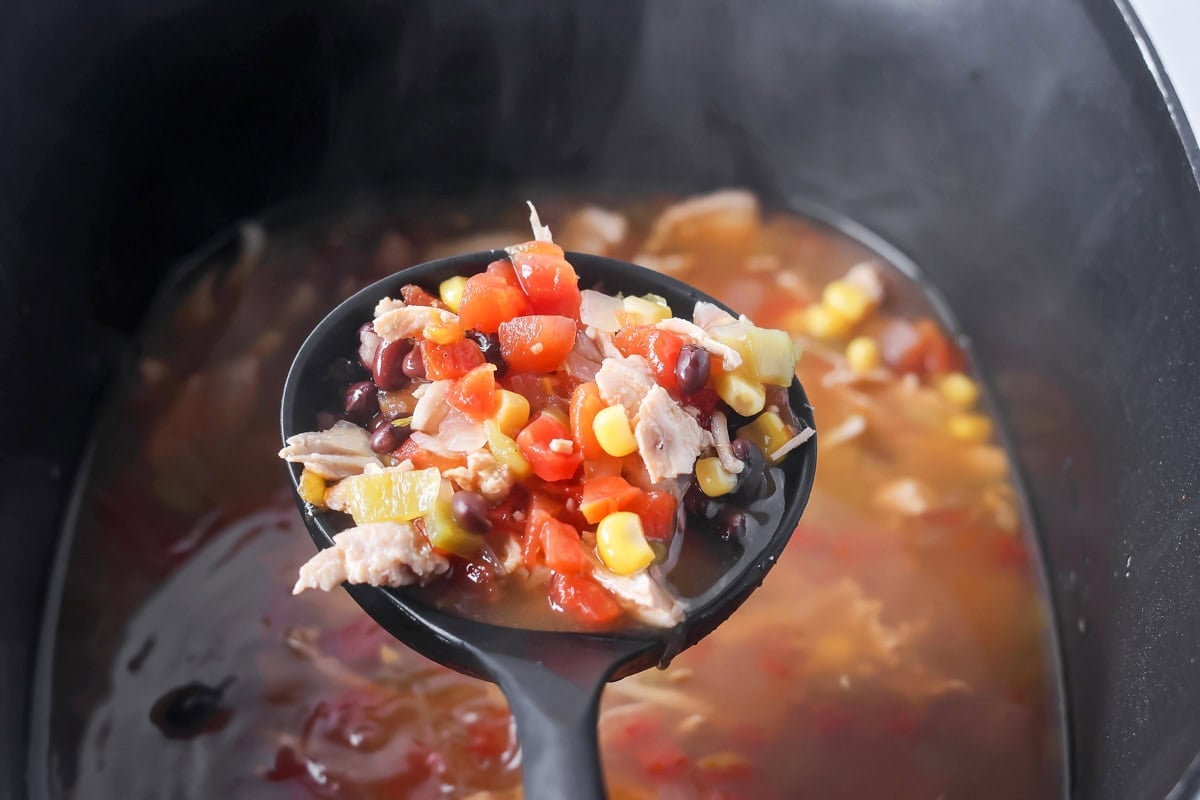 Scooping turkey tortilla soup form a crockpot.