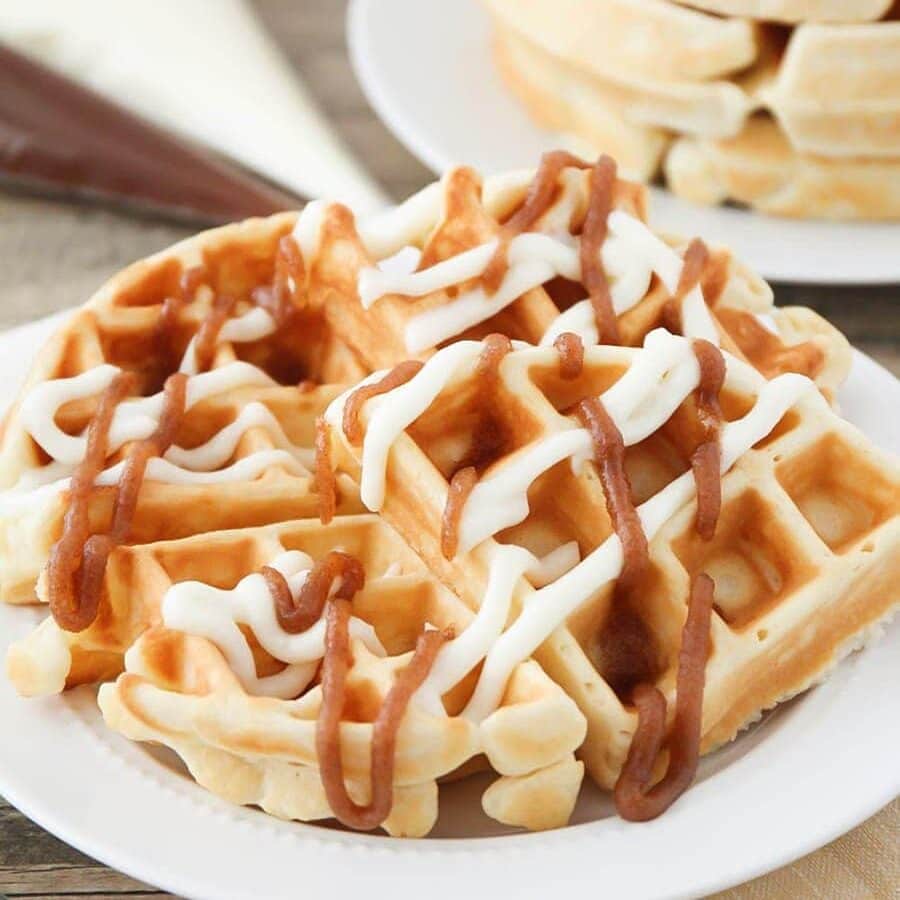 If you love breakfast foods like I do, this recipe is for you! Two of my absolute favorite breakfasts combine in these amazingly delicious cinnamon roll waffles. Cinnamon Roll Waffles with icing on white plate